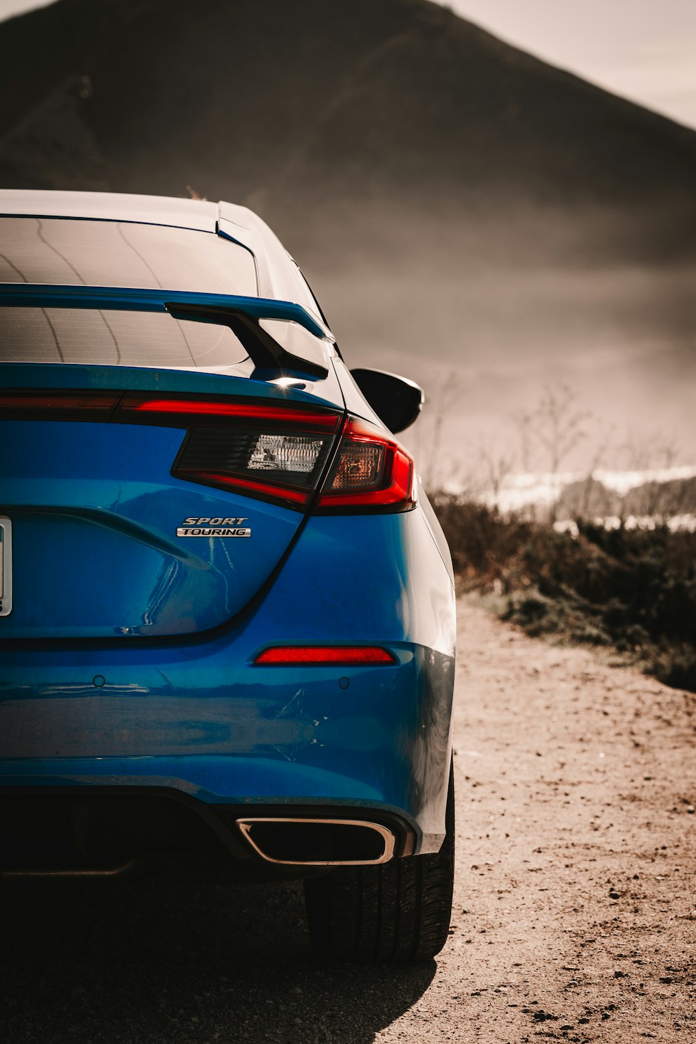 the back end of a blue car on a dirt road