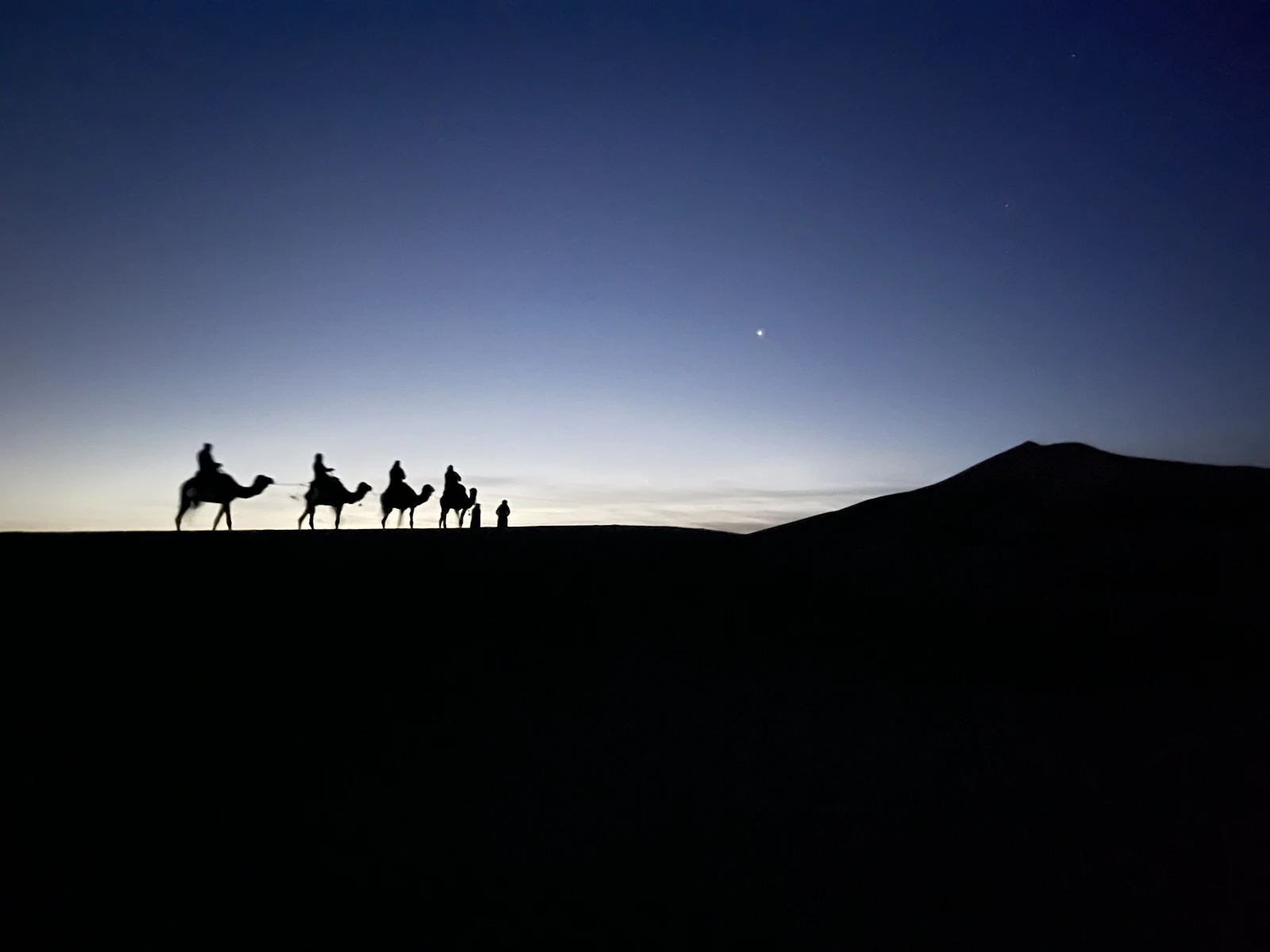 Caravana de camellos al atardecer en las dunas de Merzouga, Sahara, Marruecos