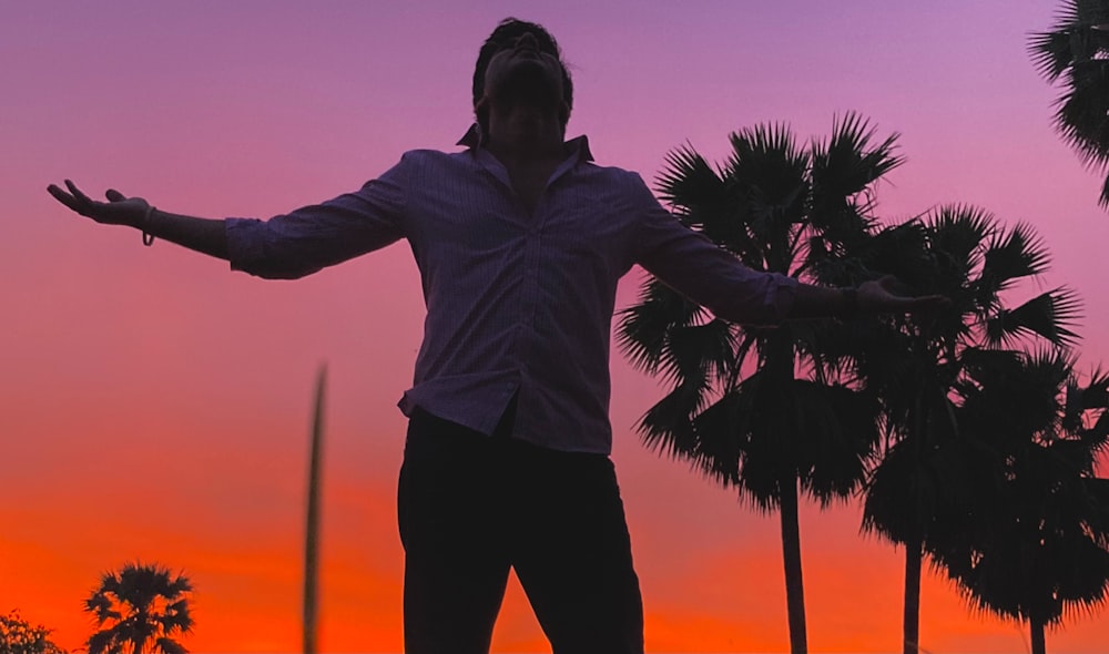 a man standing in front of a sunset with palm trees