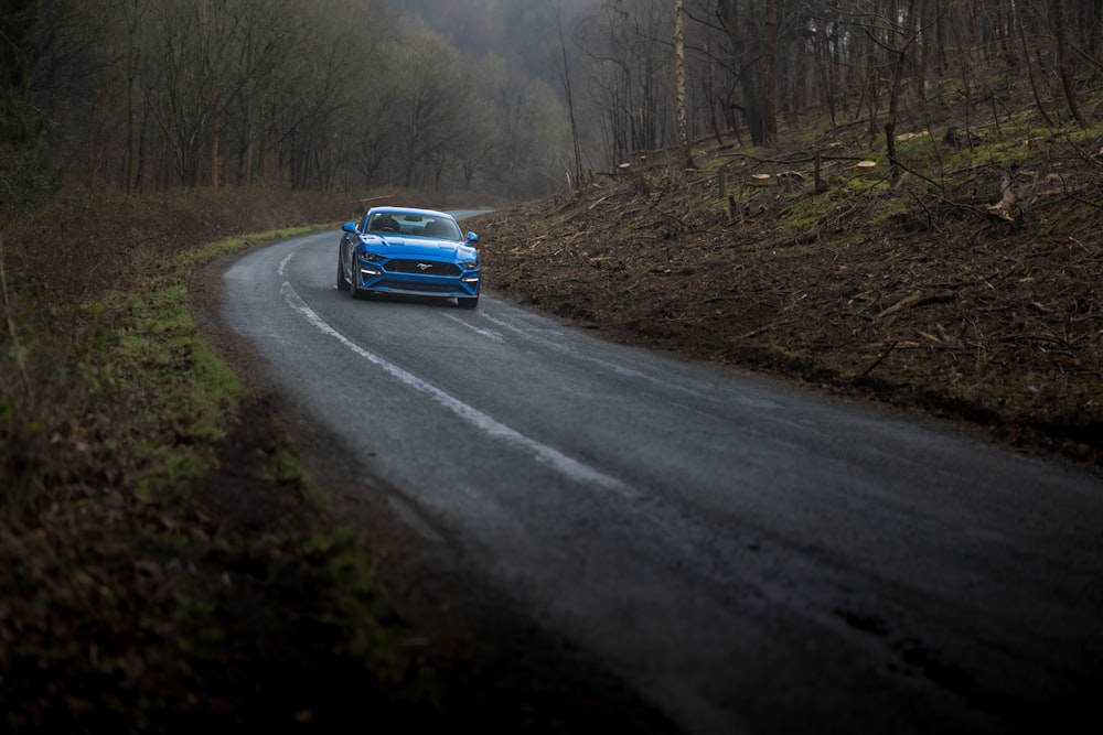 a blue sports car driving down a country road