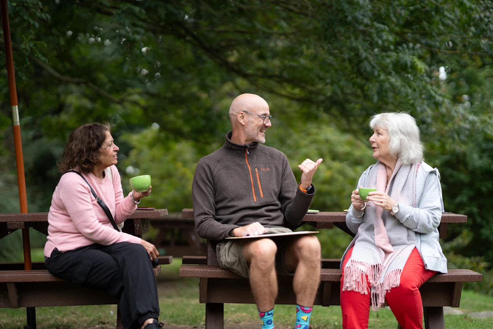 Three senior friends laughing together at an outdoor picnic table