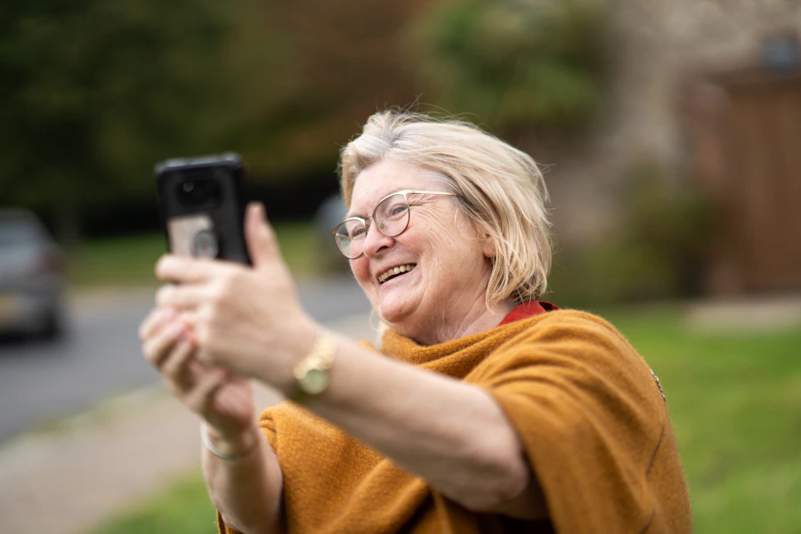 Una señora mayor sonríe mientras usa su teléfono al aire libre