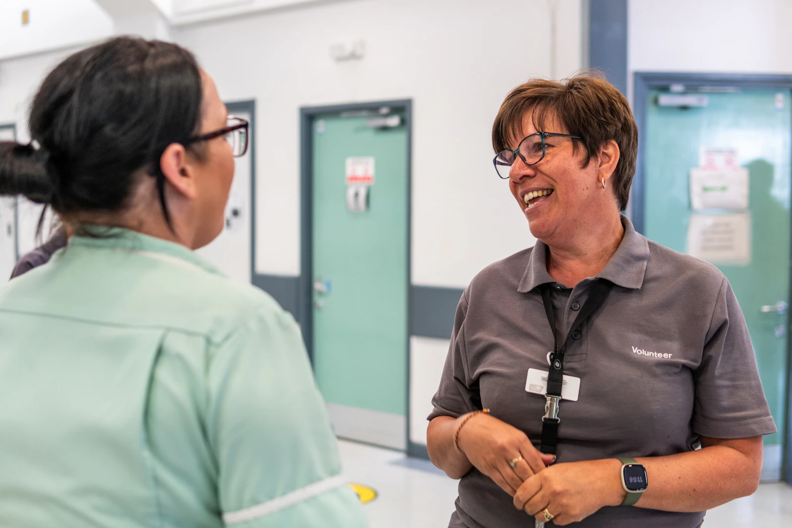 Two women in a hallway having a calm working conversation, representing the first contact between a support coordinator and a respite provider after a referral