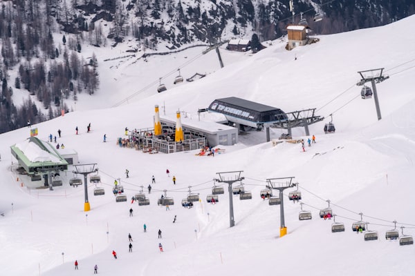 Skiers milling around a busy chairlift station on a wide snowfield with lift lines running uphill