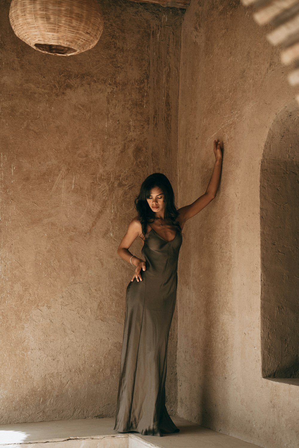 a woman in a long dress leaning against a wall