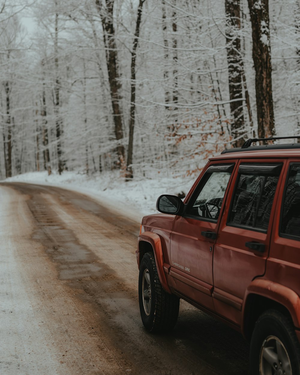 a red jeep driving down a snow covered road