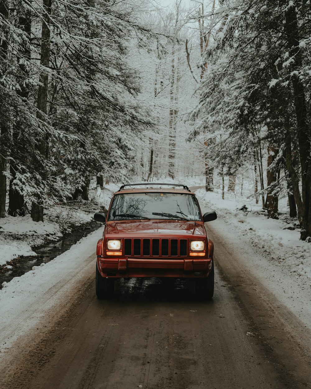 a red jeep driving down a snow covered road