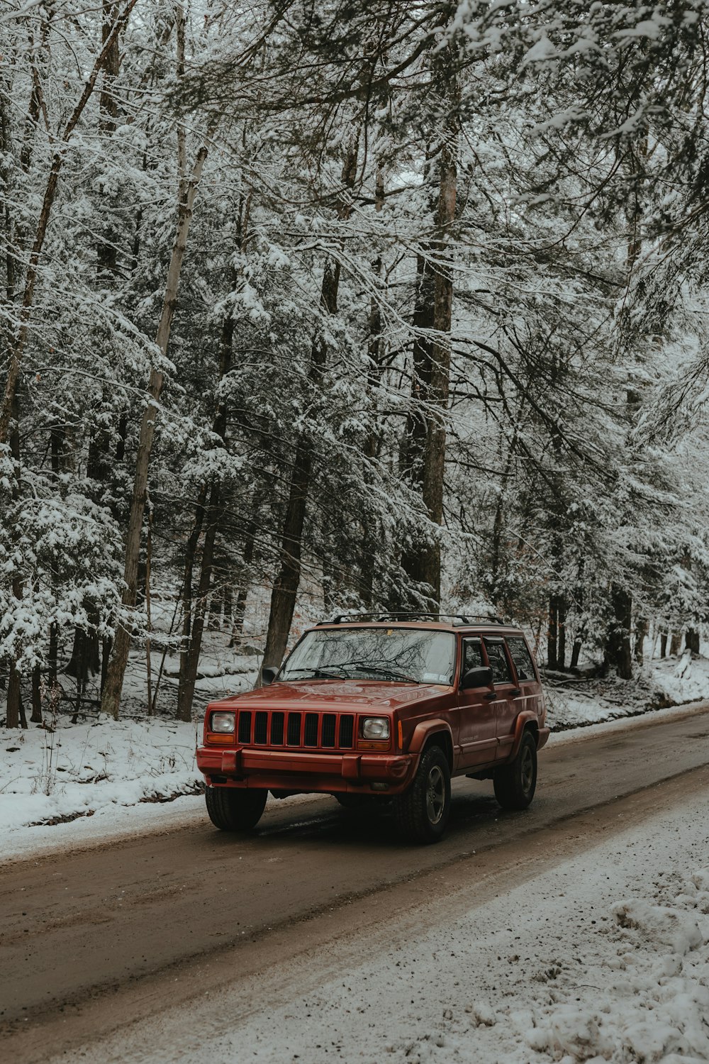 a red jeep driving down a snow covered road