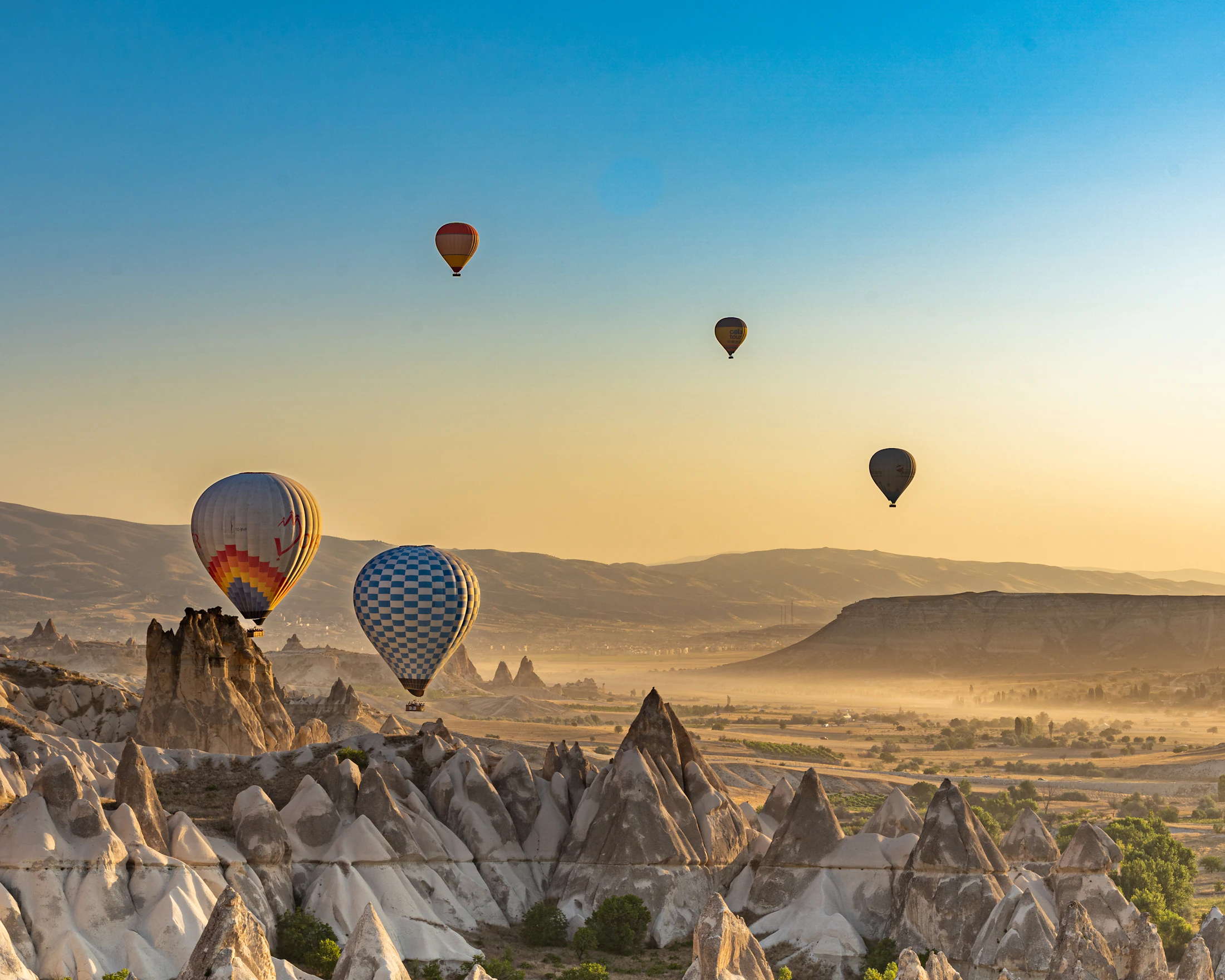 Colourful hot air balloons floating above a golden valley at sunrise
