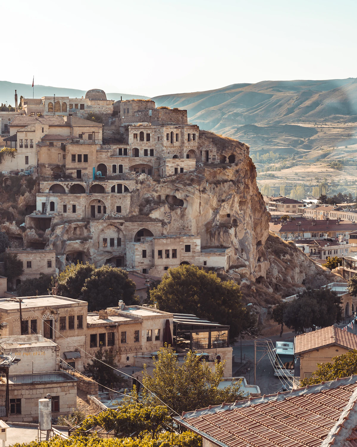 Old stone houses stacked against a rock outcrop in Ürgüp, with bare hills behind