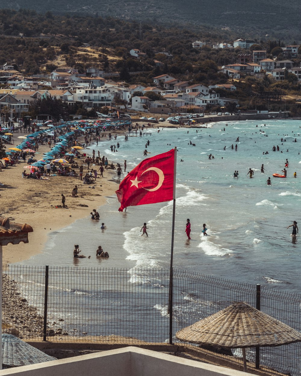 a large flag flying over a crowded beach
