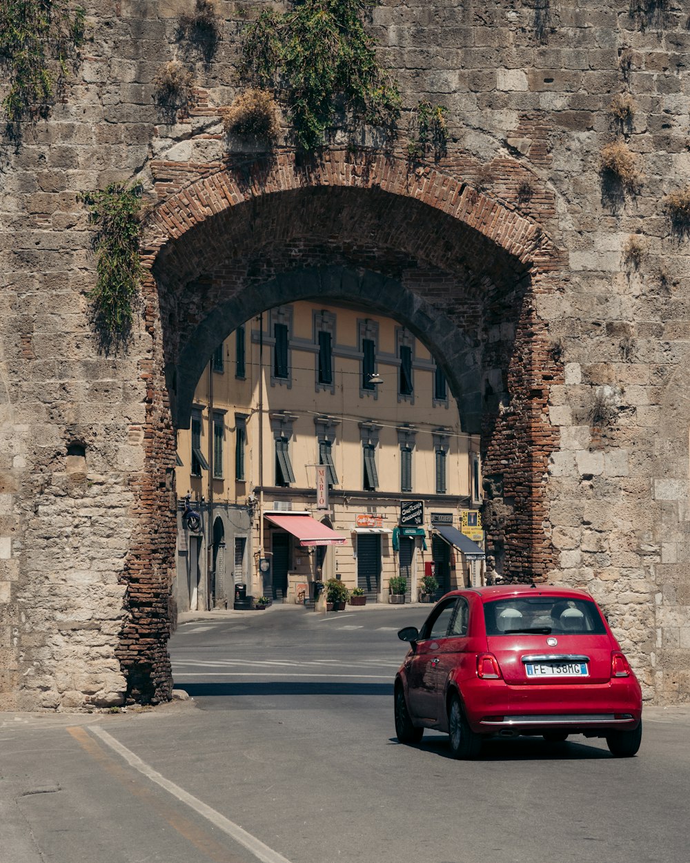 Um carro vermelho está estacionado em frente a um arco de pedra