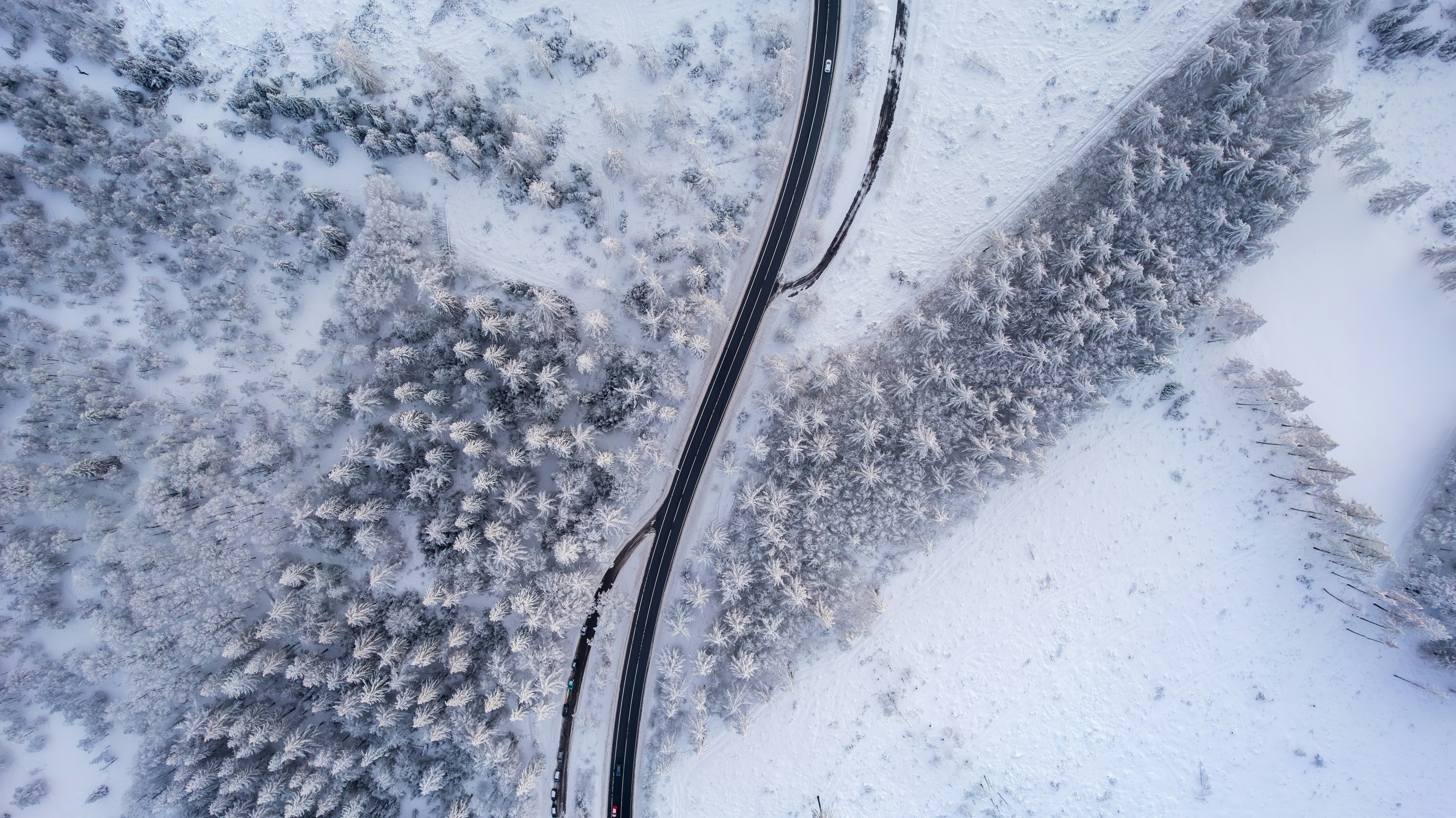 an aerial view of a road in the middle of a snow covered forest