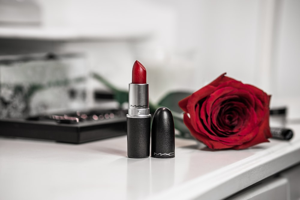 a close up of a lipstick and a rose on a table