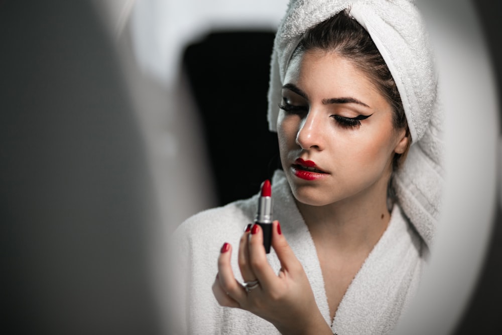 a woman with a towel on her head is putting lipstick on her face