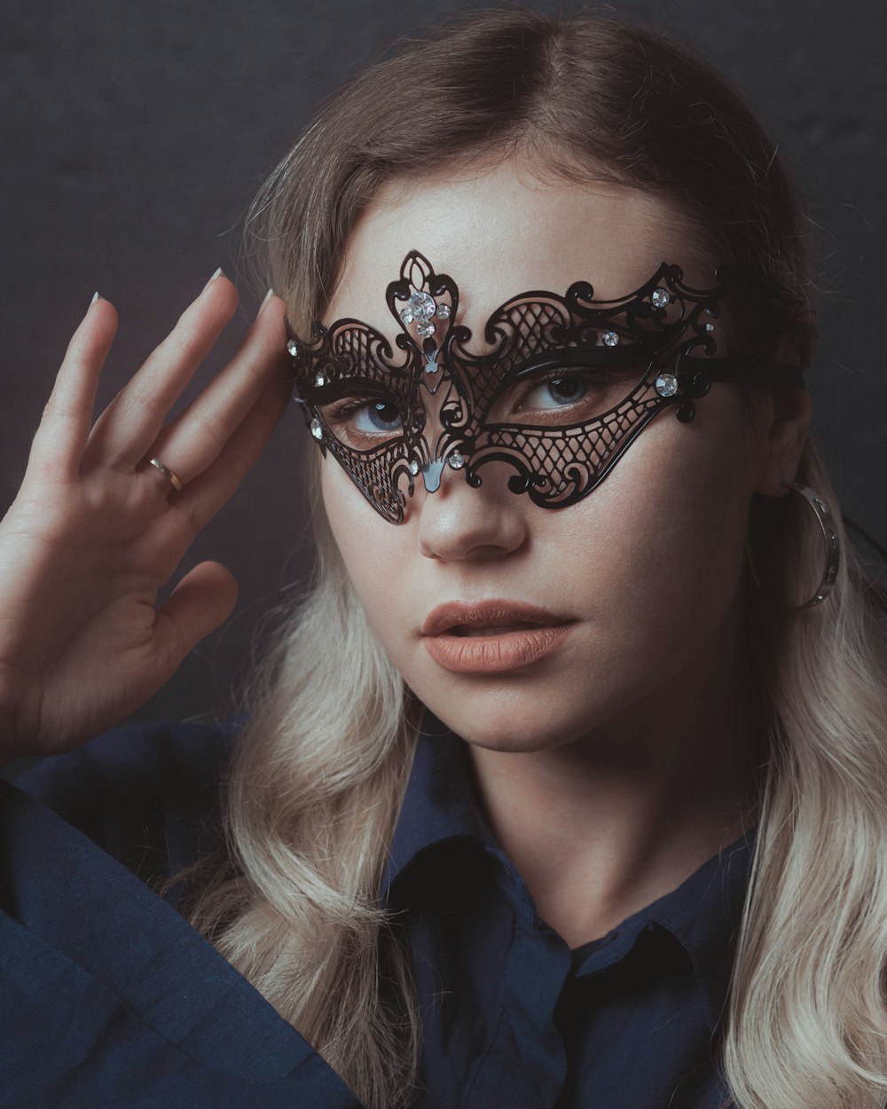 a woman wearing a black masquerade and holding her hand up to her face