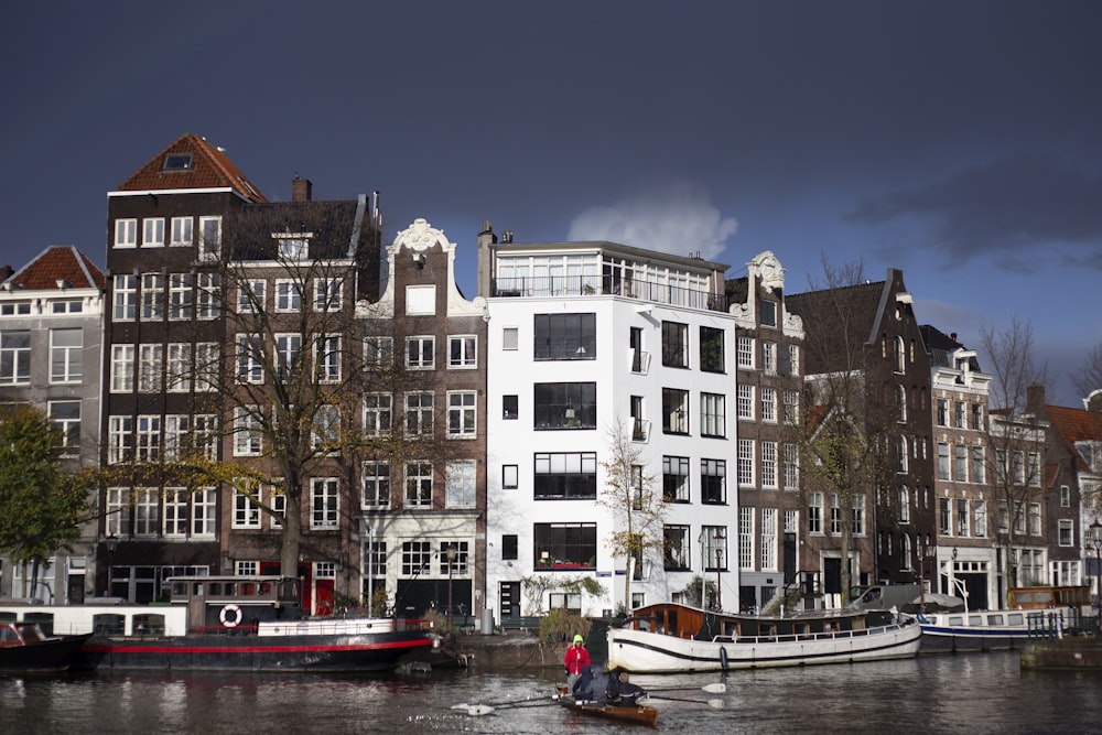 a row of boats floating on top of a river next to tall buildings