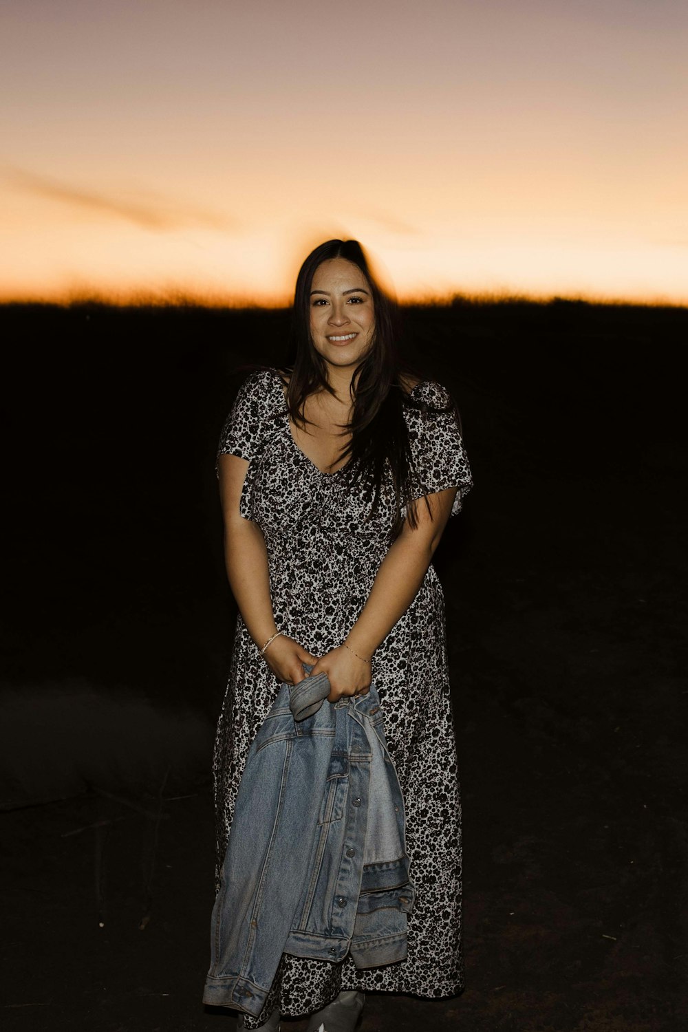 a woman standing in a field holding a jean jacket