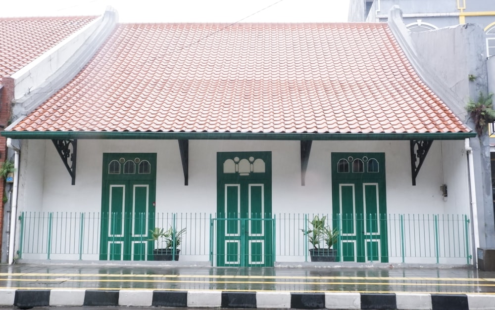 a white building with green doors and a red roof