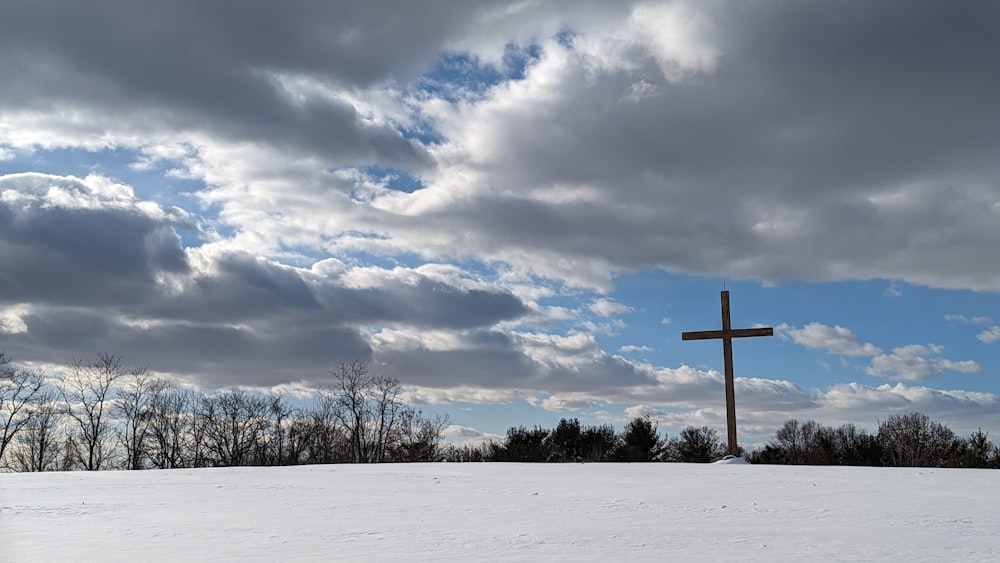 a cross on a snowy hill under a cloudy sky