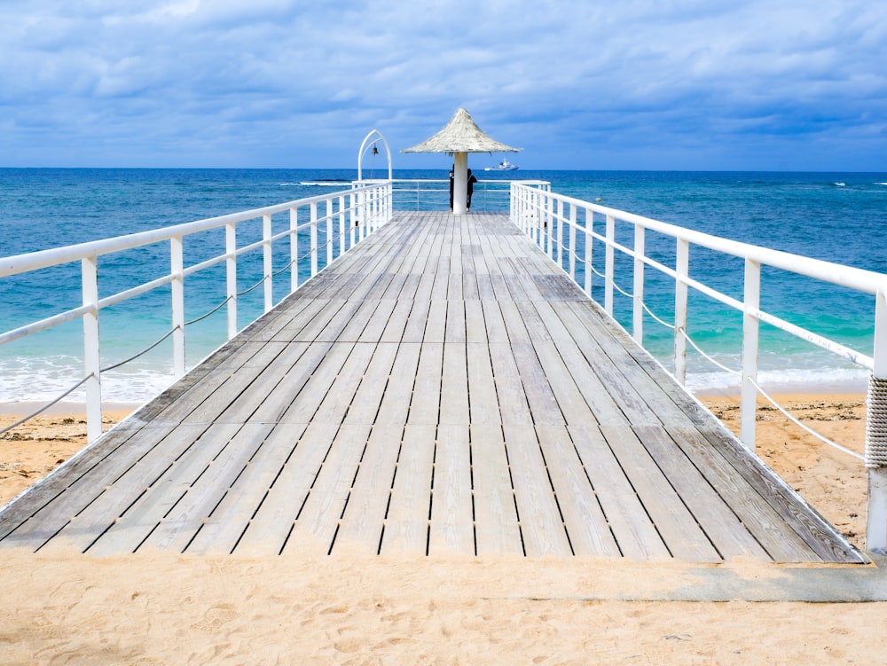 a wooden pier on the beach with a thatched umbrella