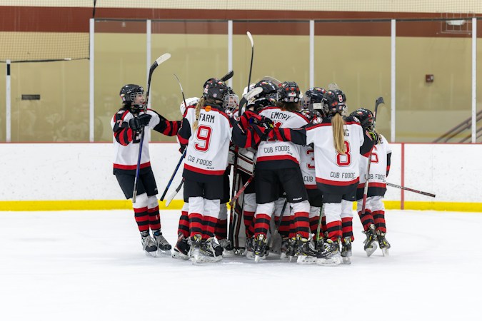 A group of young hockey players skate together during a game on an indoor rink