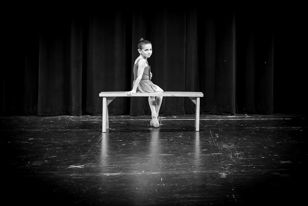 a young girl sitting on a bench in front of a curtain