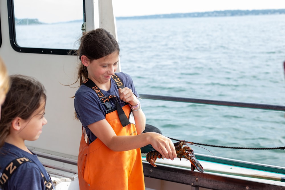 a girl in an orange apron holding a crab on a boat