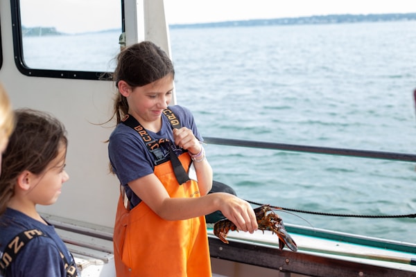 A girl in an orange apron holding a crab on a boat