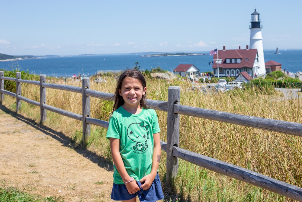 a young girl standing in front of a wooden fence