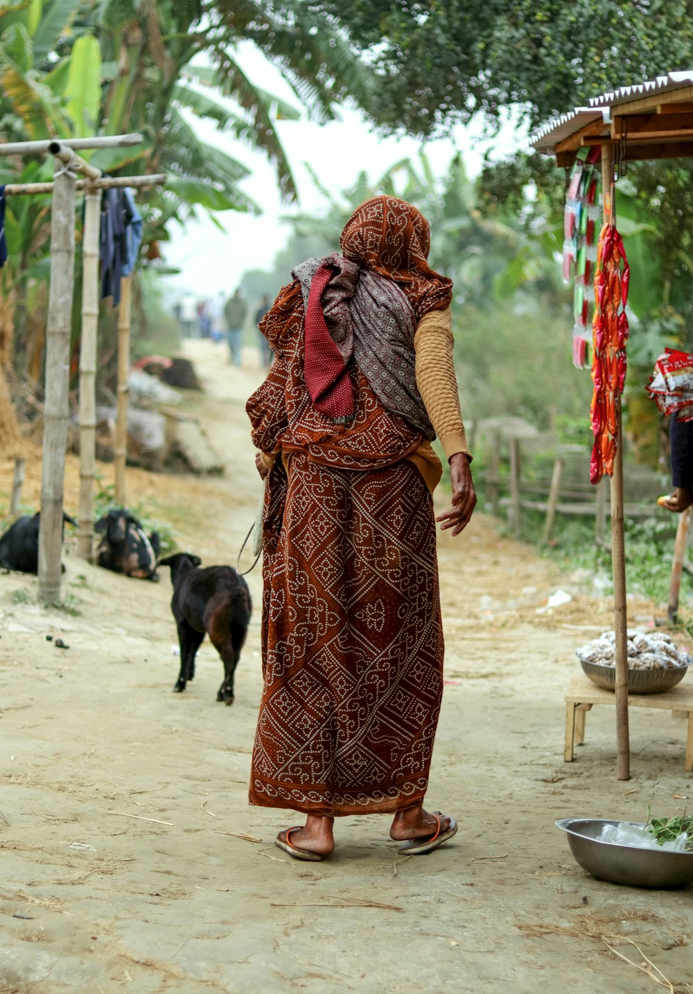 a woman walking down a dirt road next to a dog