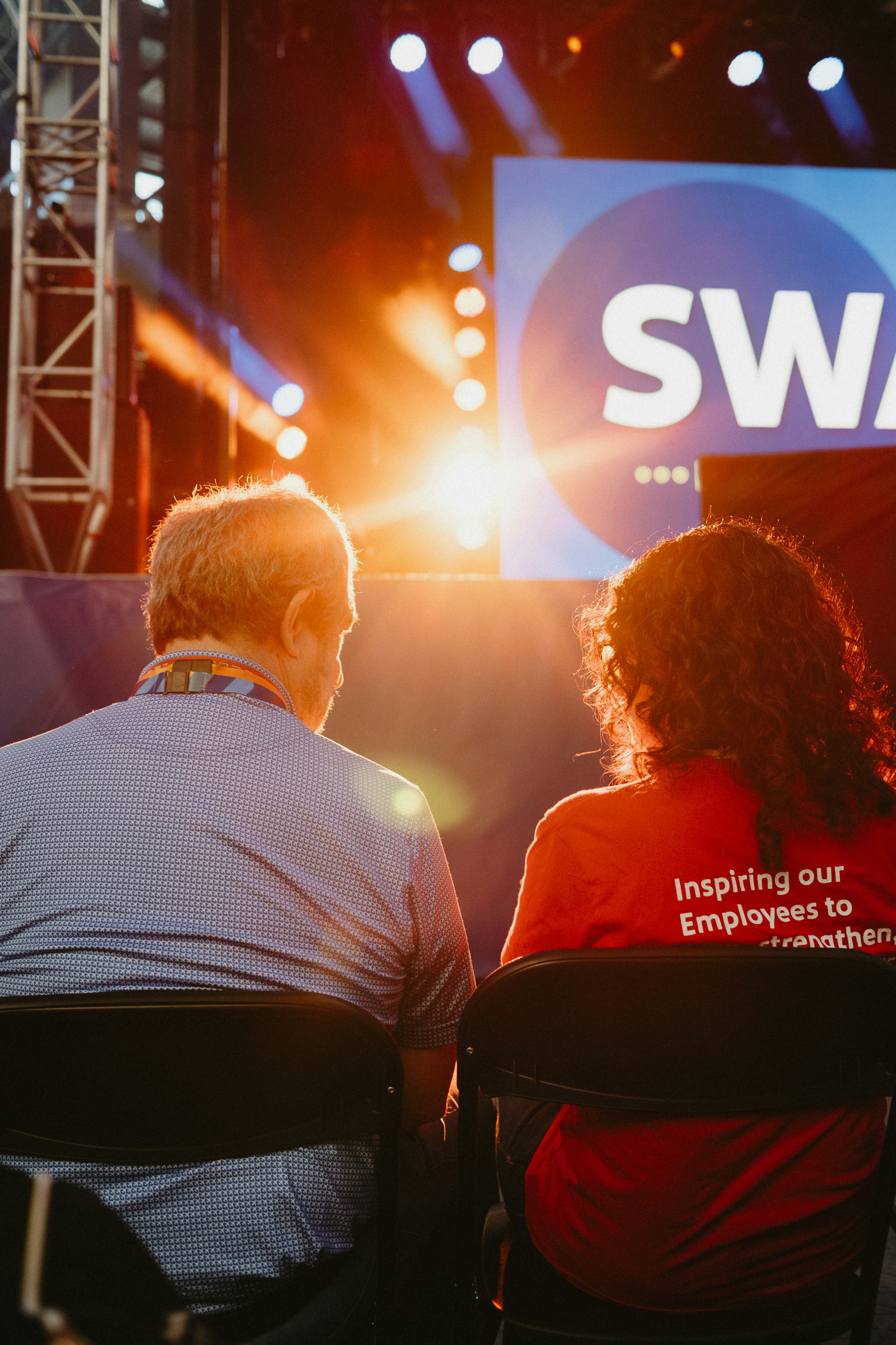 a couple of people sitting in chairs in front of a swag sign