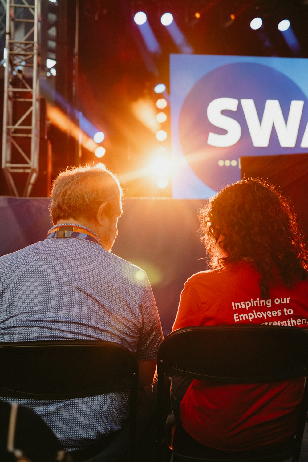 a couple of people sitting in chairs in front of a swag sign