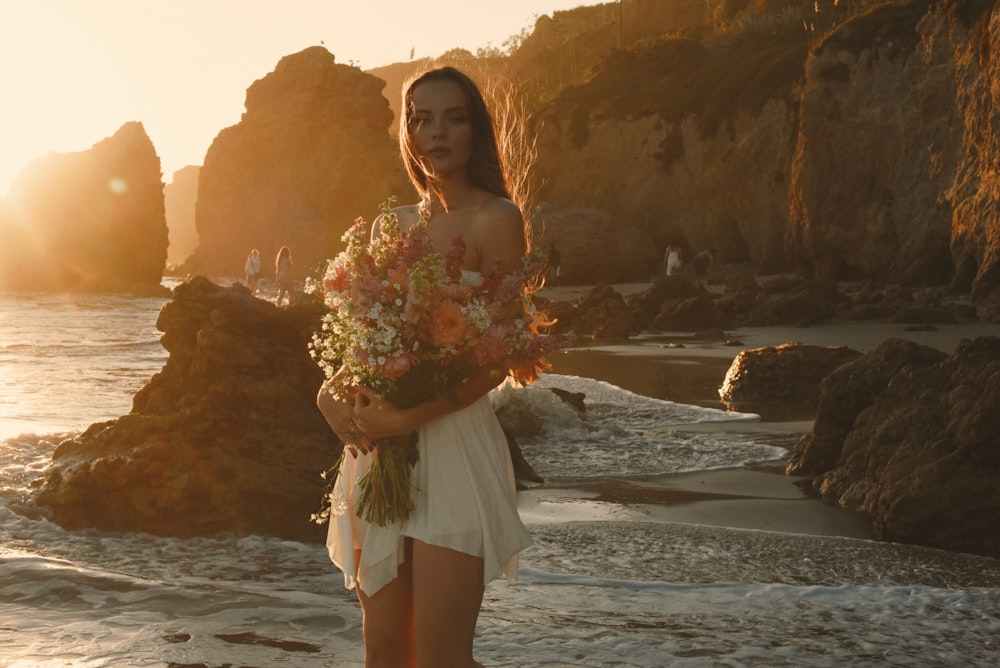 uma mulher em pé em uma praia segurando um buquê de flores