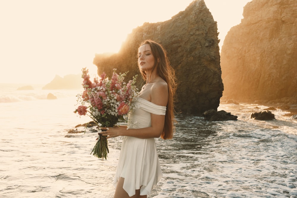 une femme en robe blanche tenant un bouquet de fleurs