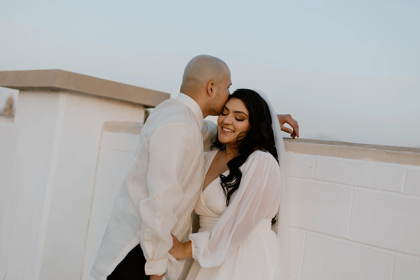 Bride and groom in formal wedding attire standing together near elegant building in timeless black and white portrait