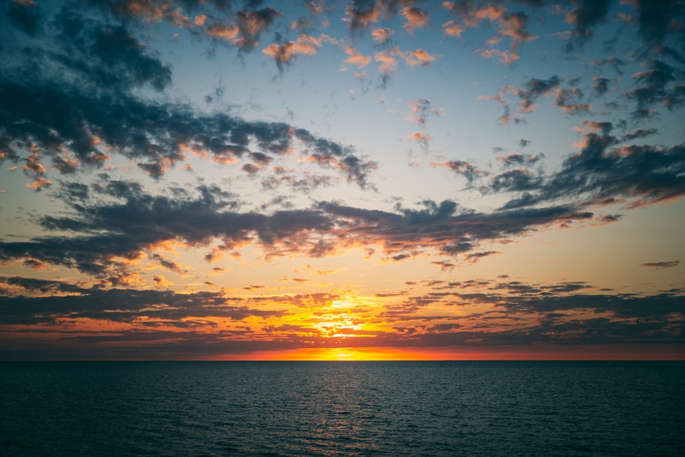 the sun is setting over the ocean on a cloudy day