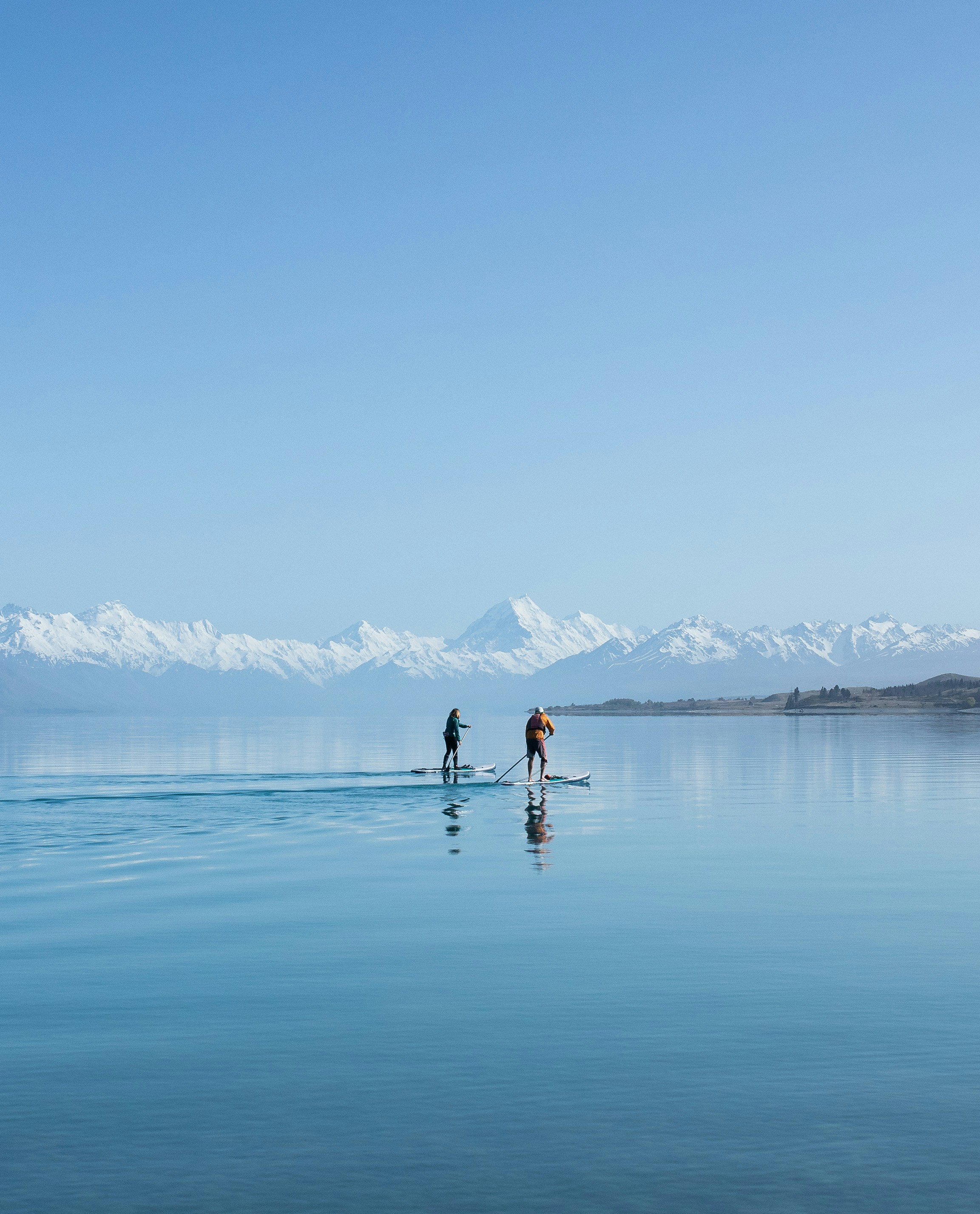 Deux personnes se tiennent debout sur des planches de surf au milieu d’un lac