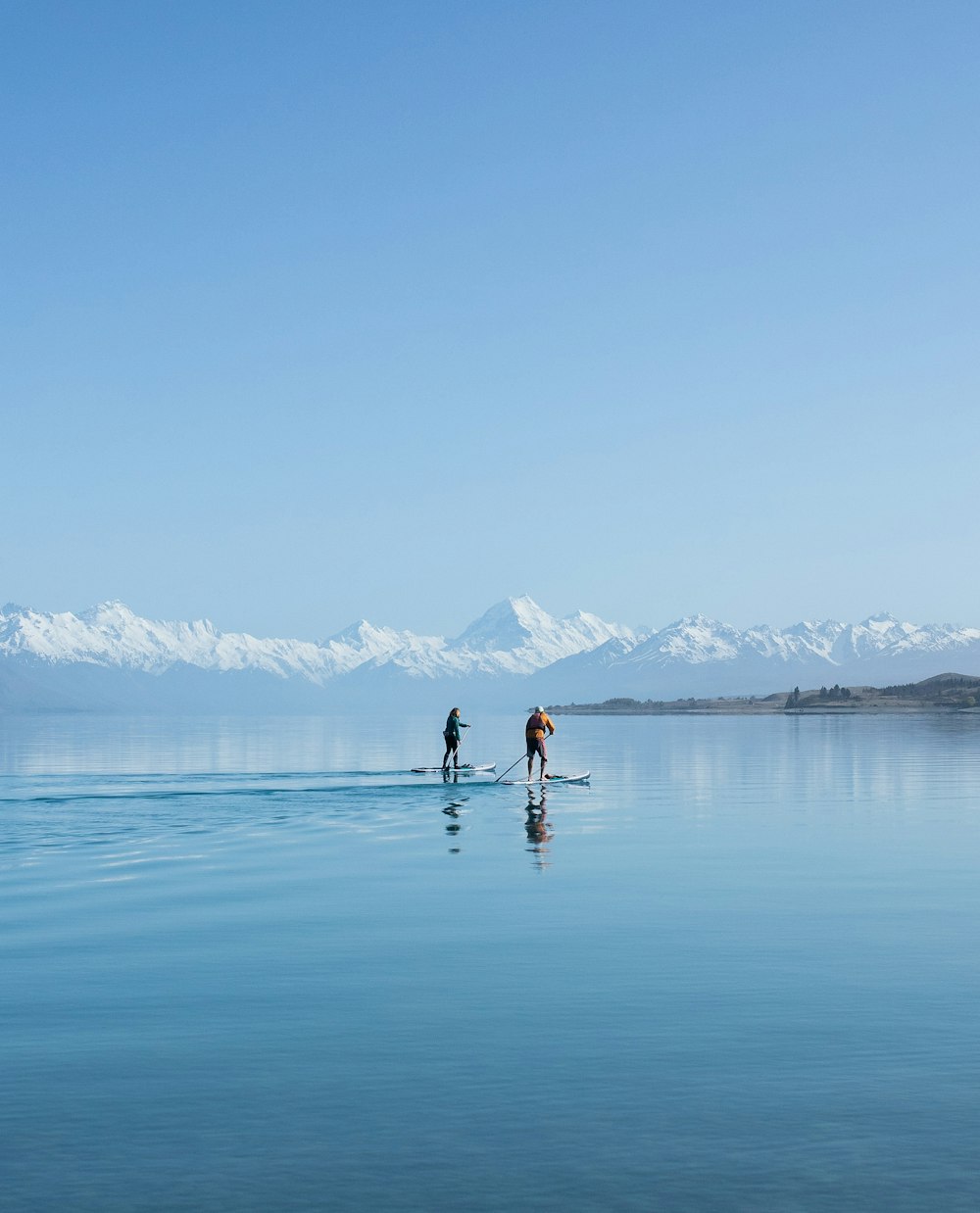 two people stand on surfboards in the middle of a lake