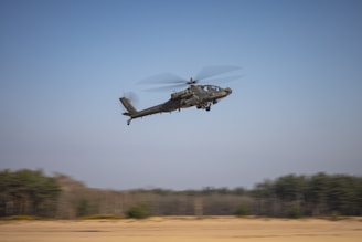 a helicopter flying over a field with trees in the background