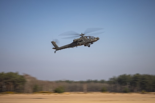 a helicopter flying over a field with trees in the background