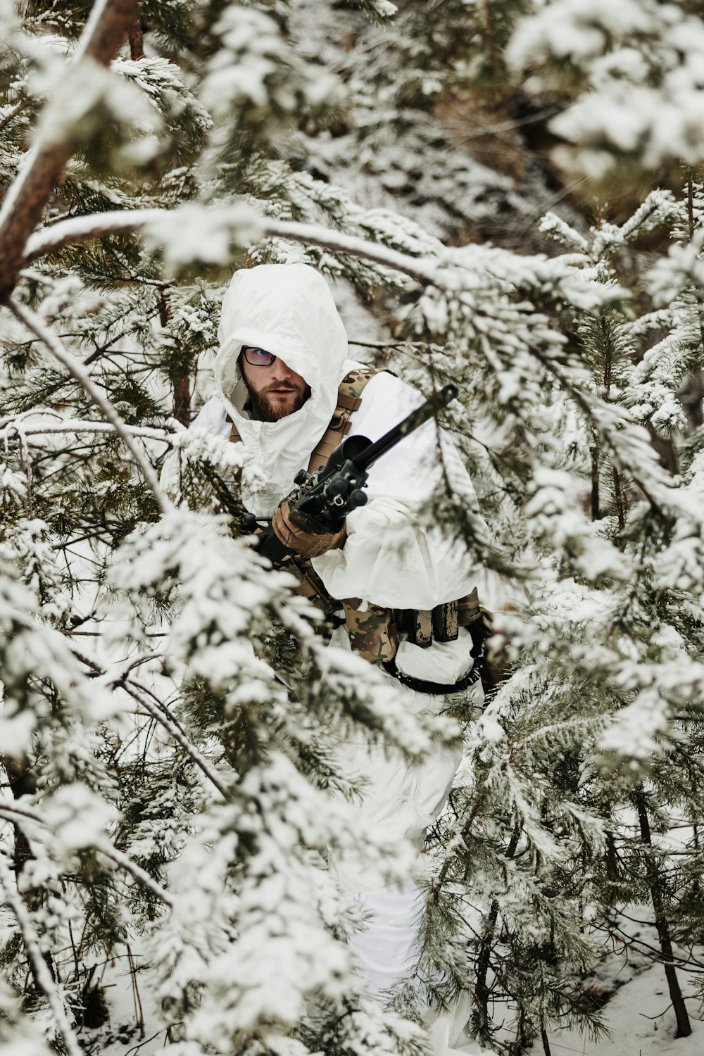 a man in a white outfit holding a gun in a snowy forest