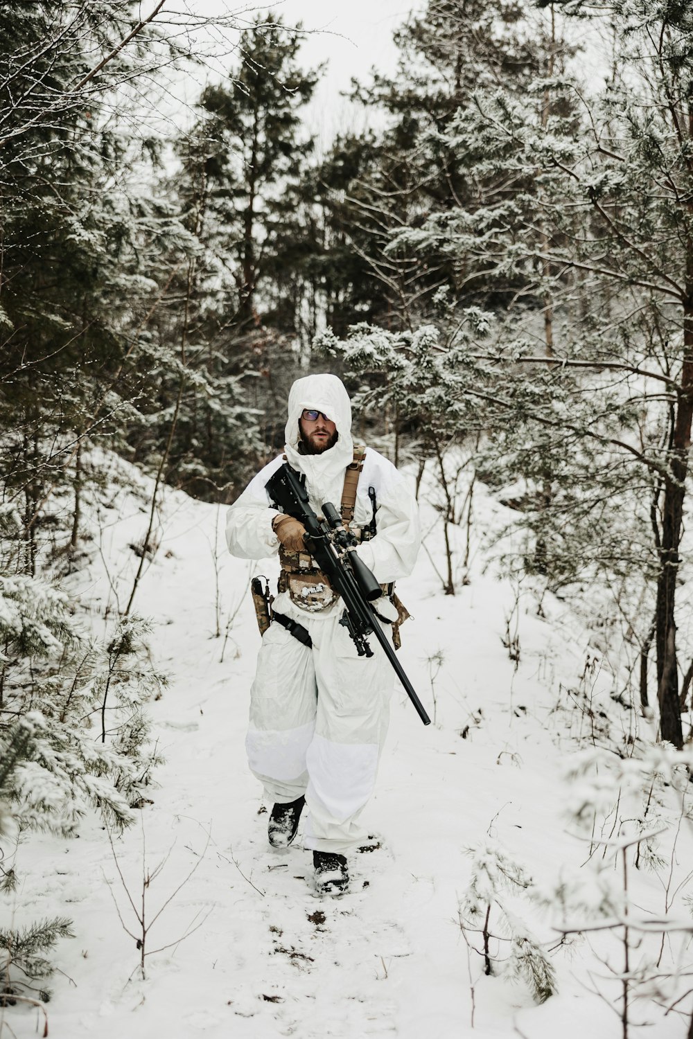 a man in a white outfit holding a rifle in the snow