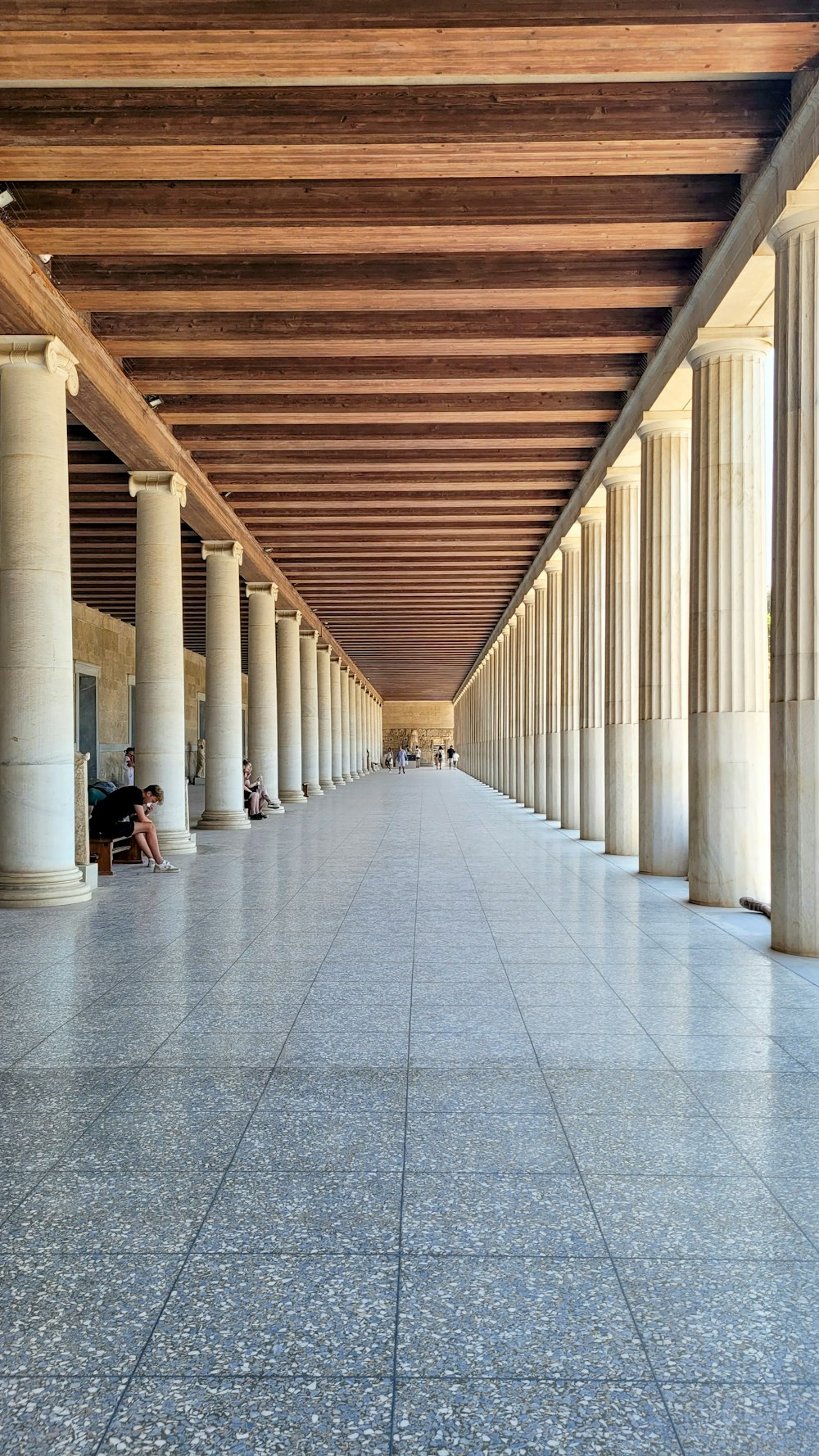 a long hallway with columns and people sitting on benches