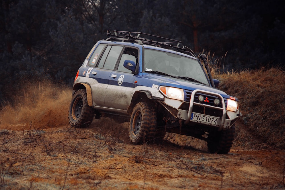 a blue four door suv driving on a dirt road