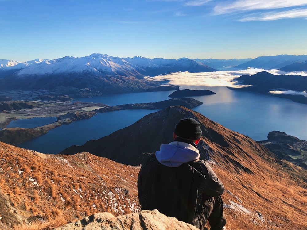 a man sitting on top of a mountain overlooking a lake