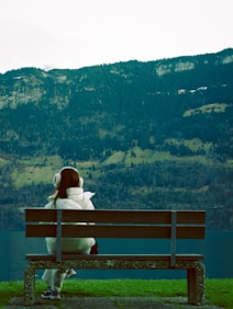 a woman sitting on a bench in front of a lake