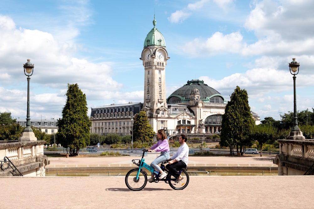 two people riding a bike in front of a building