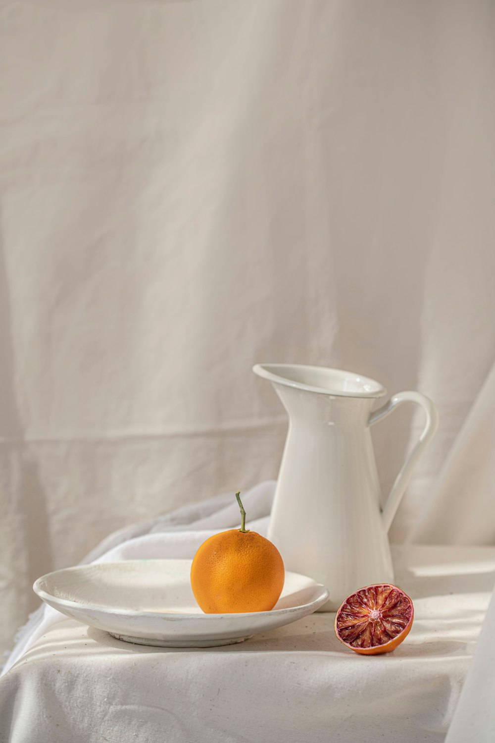 a white pitcher and a plate with an orange on it