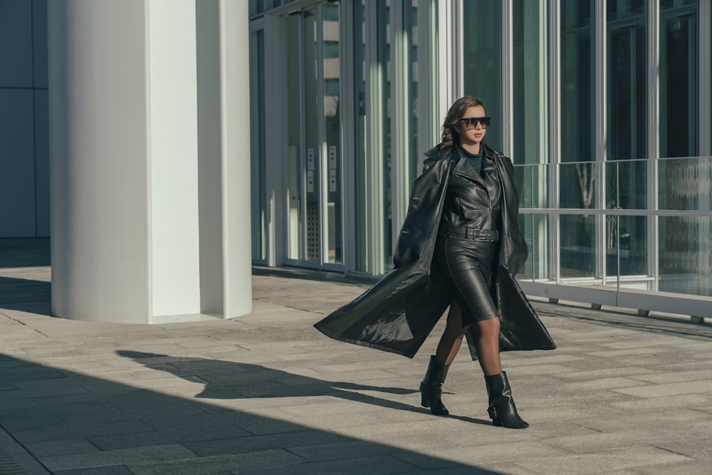 a woman walking down a sidewalk in a black coat